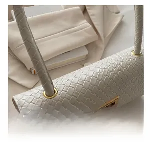 Close-up of beige baguette bag showing woven leather texture and golden metal buckle detail