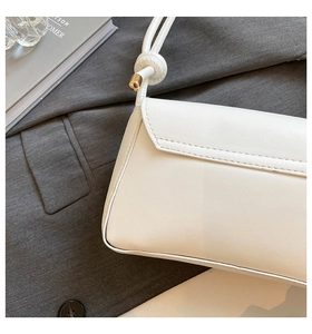 Detail of white leather baguette bag showing premium stitching and knotted strap with gold tips