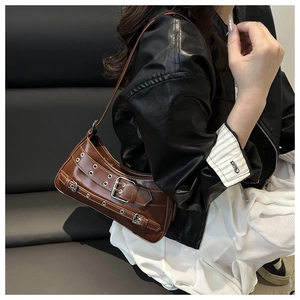 Detail of a brown crescent shoulder bag with metallic eyelets and buckles worn by a model