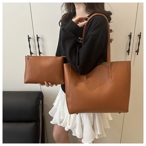 Detail of a brown leather tote bag and pouch set showing stitching and dual handles
