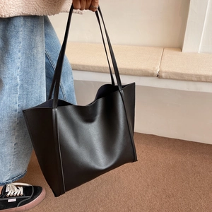 Detail of minimalist black faux leather tote bag showing smooth matte texture and shoulder strap
