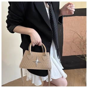 Close-up of beige trapezoid bag with silver star emblem and textured leather finish