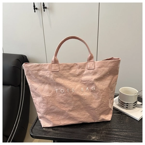 Macro detail of the light pink tote bag with crinkled texture and white TOTE BAG lettering