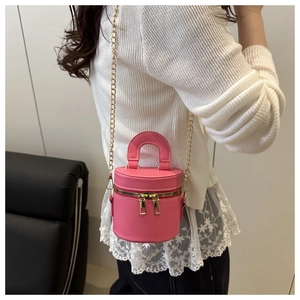 Mini sac seau cylindrique rose avec bandoulière dorée porté par un mannequin