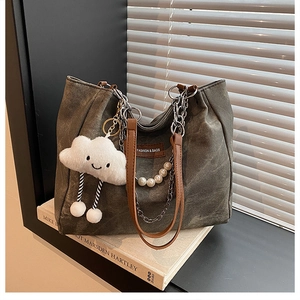 Detail of olive canvas tote with pearl chain strap and plush cloud charm on a book
