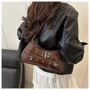 Detail of a brown leather baguette bag with silver eyelets and buckles in punk style