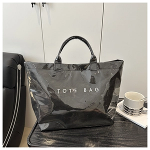 Close-up of a black glossy tote bag with white TOTE BAG text in a minimalist setting
