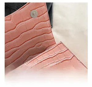 Detail of pink croc-embossed leather texture and round magnetic metal clasp of the bag