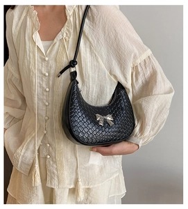 Detail of black woven crescent bag featuring a silver metal bow and slim leather shoulder strap