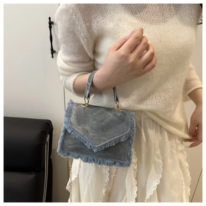 Detail of denim crossbody bag featuring fringe trim, triangle flap and gold metal handle