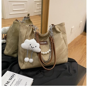 Detail of khaki tote bag featuring silver chain, pearls, and a plush cloud charm
