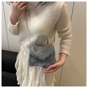 Close-up of gray denim crossbody bag with fringe edges and elegant gold chain strap