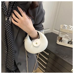 Detailed close-up of white crescent bag with gold chain strap and magnetic metal clasp
