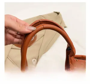 Detail of a brown leather tote bag showing semi-circular handles and leaf embossing