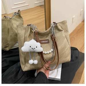 Detail of canvas tote bag with pearl chain, brown leather logo, and plush cloud charm