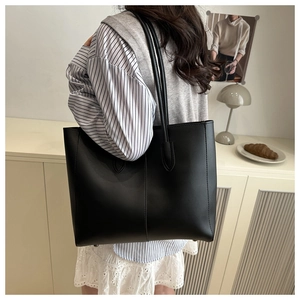 Detail of minimalist black tote bag with vertical stitching and reinforced shield handles