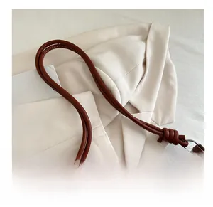 Detail of a brown leather cylindrical rope strap with decorative knot and silver buckle