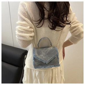Close-up of light blue denim mini crossbody bag with frayed edges and gold chain strap