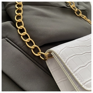 Détail d'un sac blanc à motif crocodile avec une chaîne dorée épaisse et stylée
