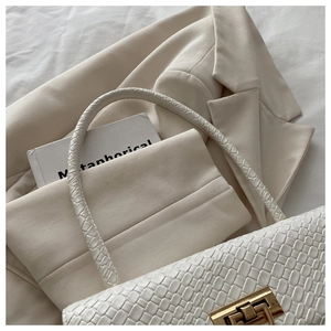 Close-up of beige woven texture shoulder bag with elegant gold buckle on a blazer
