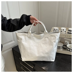 Detail of white glossy tote bag with embossed TOTE BAG text and crinkle texture