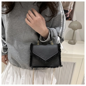 Detail of a black mini fringed handbag with elegant gold chain and top handle