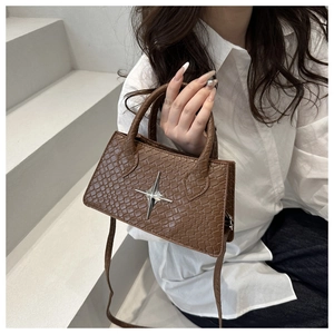 Detail of a brown crocodile-patterned square bag with silver star hardware shown on a model