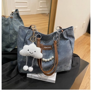 Detail of blue denim tote bag with brown leather handles, pearl strap and fluffy charm