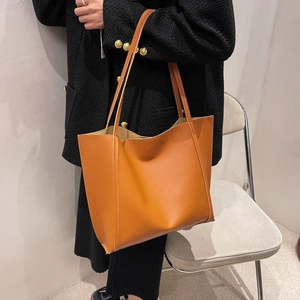 Brown leather tote bag worn by a model in a tweed coat, showing the large capacity size