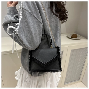 Detail of black faux leather bag with V-shaped flap, fringe trim and gold chain strap