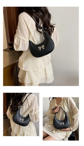 Detail of black crescent shoulder bag with woven texture and silver bow decoration