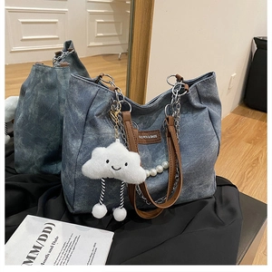 Detail of blue denim tote bag with brown leather handles and plush cloud charm