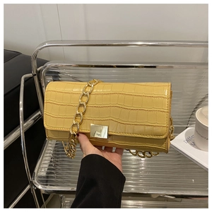 Détail d'un petit sac carré jaune à texture crocodile avec une large chaîne dorée