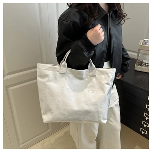 Detail view of pearl white tote bag with embossed text and glossy wrinkled texture