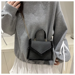 Detail of black mini square bag featuring fringe edges and a sleek gold chain strap
