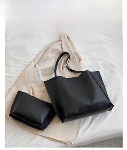 Detail view of large black faux leather tote bag with matching zippered pouch on blazer