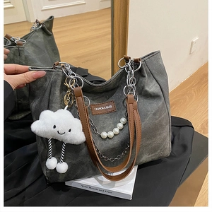 Detail of grey canvas tote bag with brown leather straps and pearl chain charm