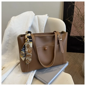 Dettaglio di una borsa tote in pelle marrone con foulard floreale vintage su sedia