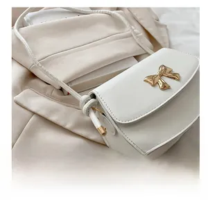 Détail du petit sac blanc en cuir avec fermoir nœud doré posé sur une veste beige
