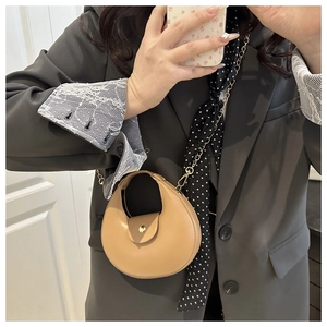 Detailed close-up of light brown crescent handbag featuring gold chain and magnetic clasp
