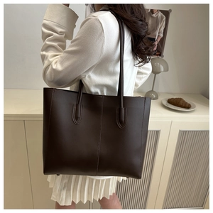 Detail of dark brown leather tote bag showing vertical seam design and long shoulder straps