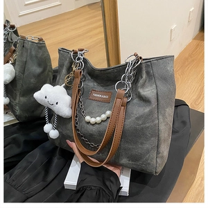 Detailed view of grey canvas tote bag with brown leather handles and pearl chain charm