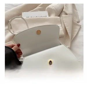Gros plan du fermoir magnétique doré sur le sac à rabat minimaliste en cuir blanc