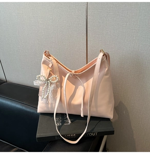 Detail of light pink leather tote bag with elegant pearl lace bow charm and strap