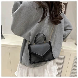 Detail of a black leather envelope bag with tassel edges and a thin metal chain strap