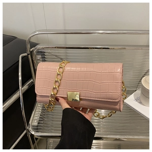Détail d'un sac à main rose en cuir croco avec chaîne dorée et fermoir rotatif en métal