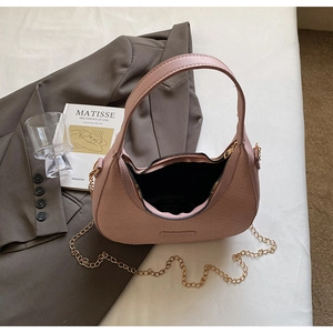Detailed overhead view of a mauve woven crescent bag with gold chain on casual bedding