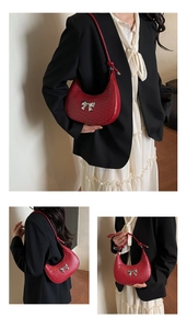 Detail of red woven crescent bag featuring a silver metal bow buckle and slim shoulder strap