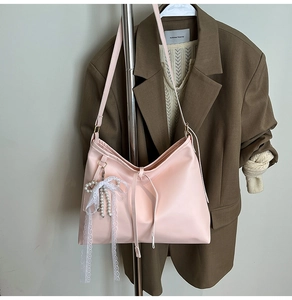 Detail of pink faux leather tote bag featuring a white lace bow and pearl tassel charm