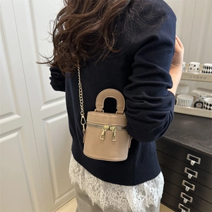 Schicke beige Mini-Eimertasche mit Goldkette, getragen von einem Model im Innenraum